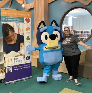 A woman is pictured with the animated character, Bluey, at a library.
